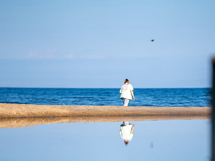 woman walking shoreline with reflection in water