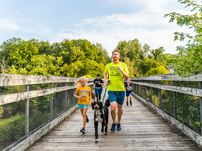 family running on trail bridge with leashed dog