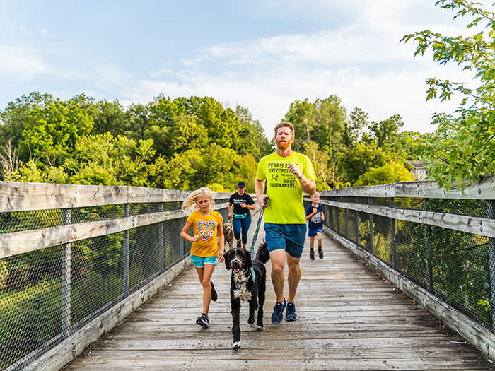 family running on trail bridge with leashed dog