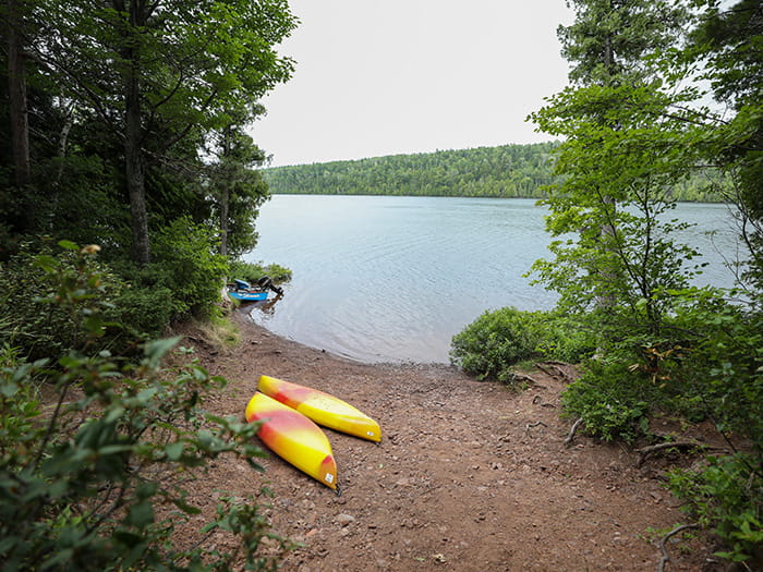 two kayaks sitting on lakeshore surrounded by trees