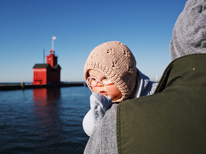 child being held by parent with big red lighthouse in background