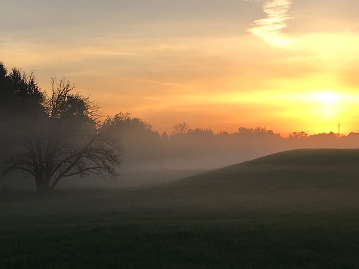 sunrise with fog above hilly landscape