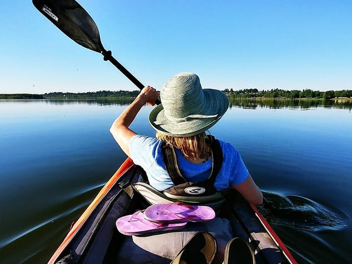 backside of kayaker with brimmed hat paddling