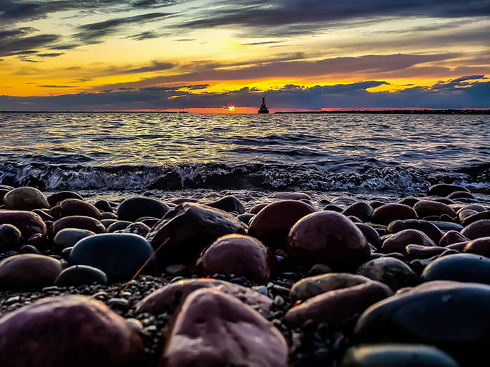 looking over rocks on shore to water and lighthouse