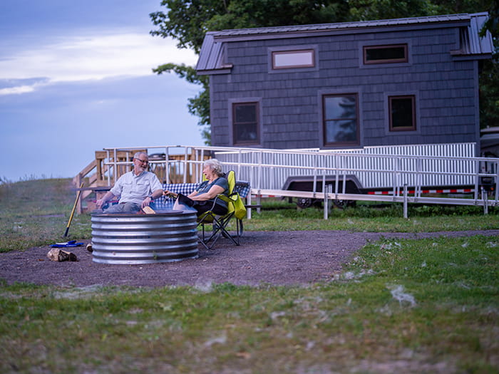 two camper sitting at fire in front of tiny house