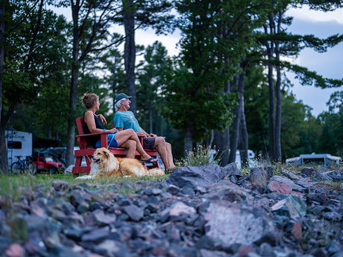 two campers sitting on bench with dog in campground