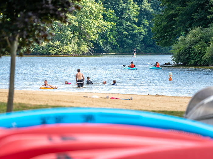 kayaks resting on shoreline with swimmers in lake