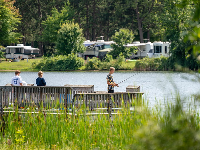 three anglers fishing from fish pier with campers on other side of lake