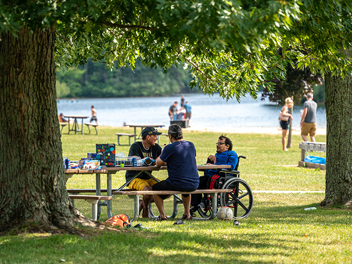 three visitors sitting at picnic table with lake in background