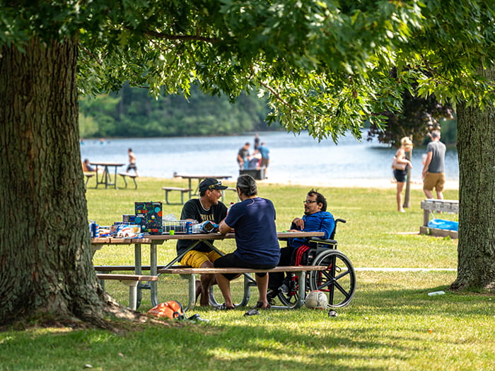 three visitors sitting at picnic table with lake in background