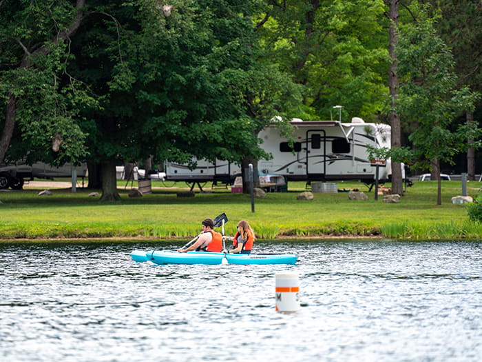 two kayakers in lifejackets with camper in background