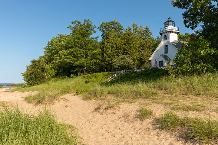 A path cuts through dune vegetation in front of a historic lighthouse at Old Mission State Park.