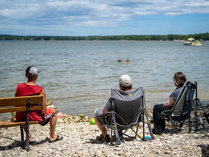 visitors sitting on rocky beach looking at lake
