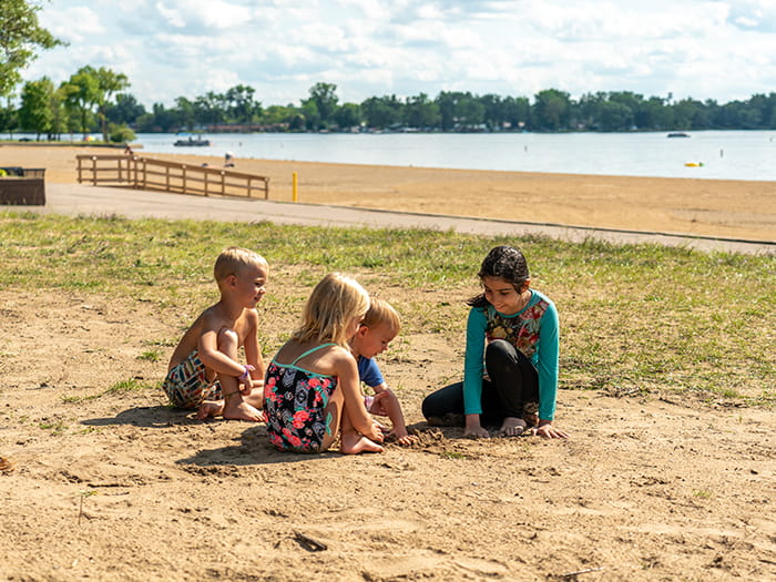 four kids playing in sand with lake in the background