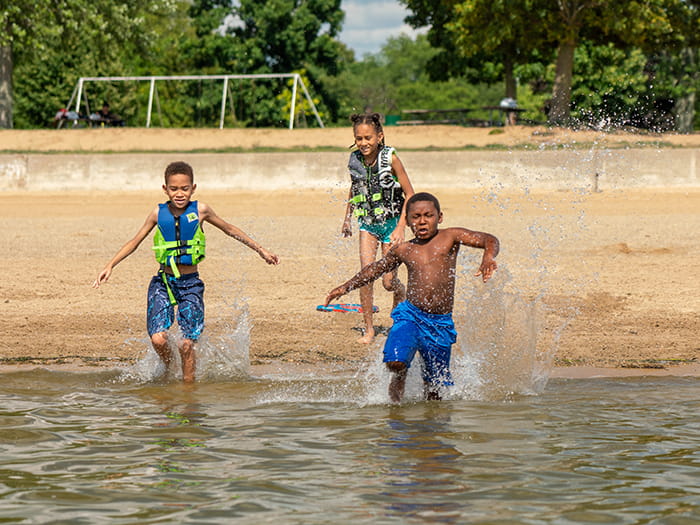 three kids running into water from sandy area