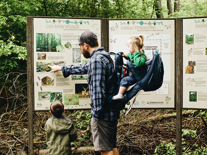 father and children looking at trailhead sign