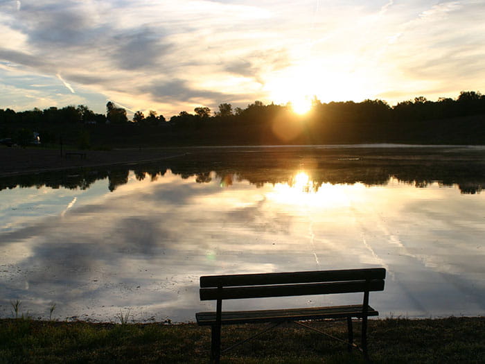 a bench along lake with sun setting in background