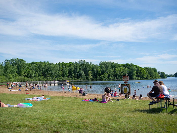 visitors swimming and sun bathing on sandy beach and green space next to lake