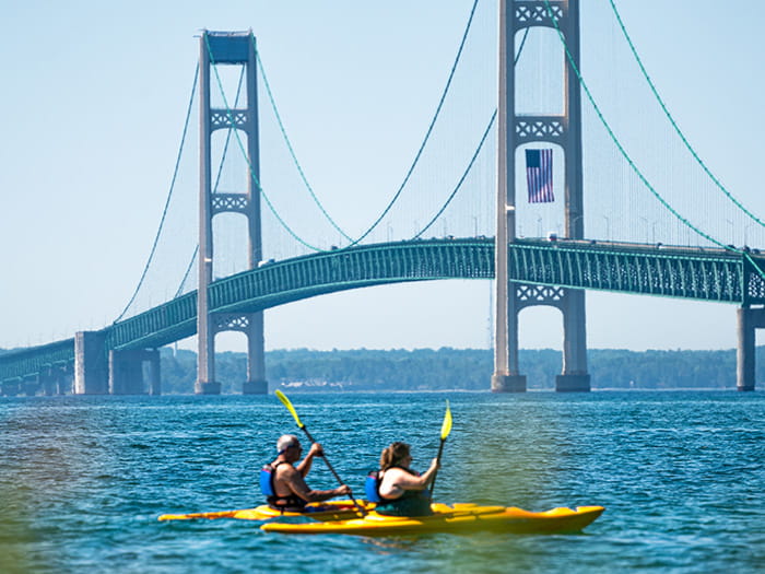 A man and woman kayaking in the straits with the Mackinac Bridge in the background