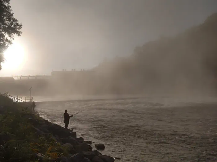 angler in river front of dam with fog