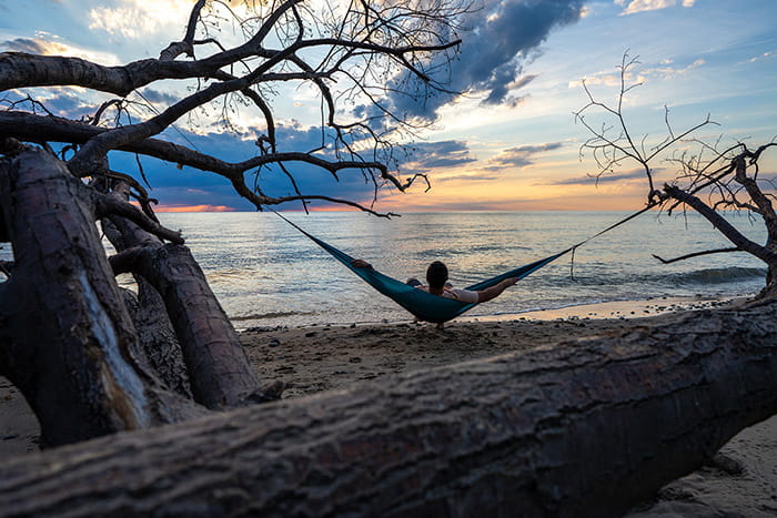 A person in a hammock on a sandy beach watching the sunset over Lake Michigan