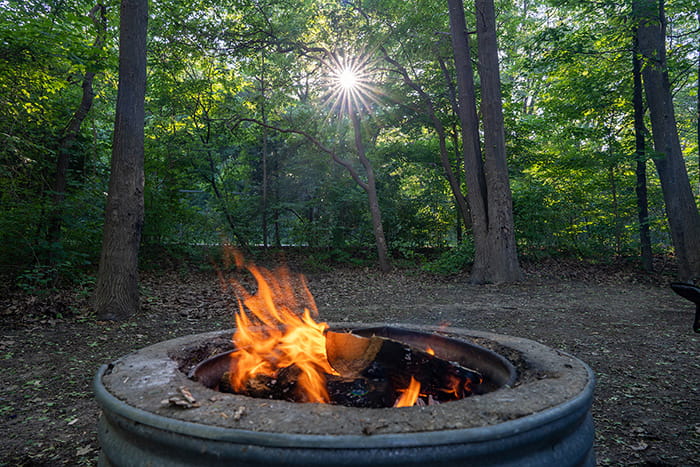A wooded campsite with a fire burning in the fire ring