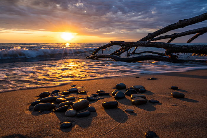 The sunset over Lake Michigan viewed from a sandy beach with rocks and downed trees