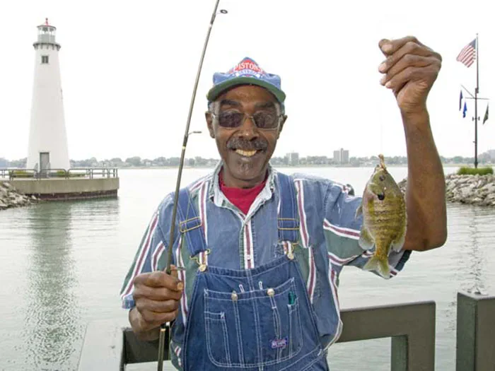 fisherman holding fish and rod with lighthouse in background