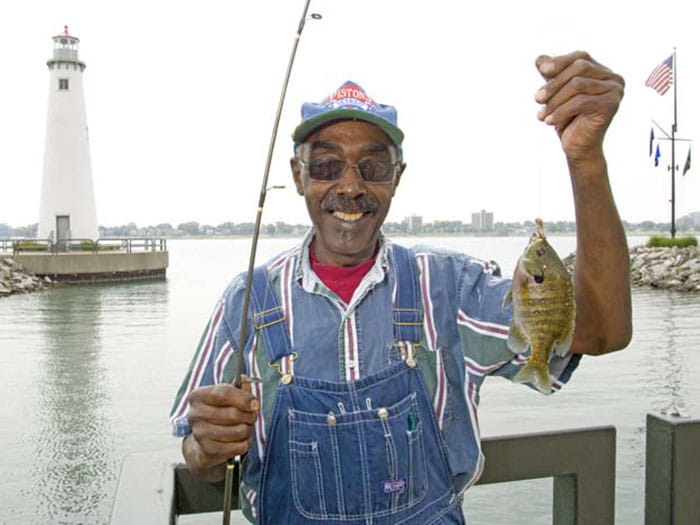 fisherman holding fish and rod with lighthouse in background
