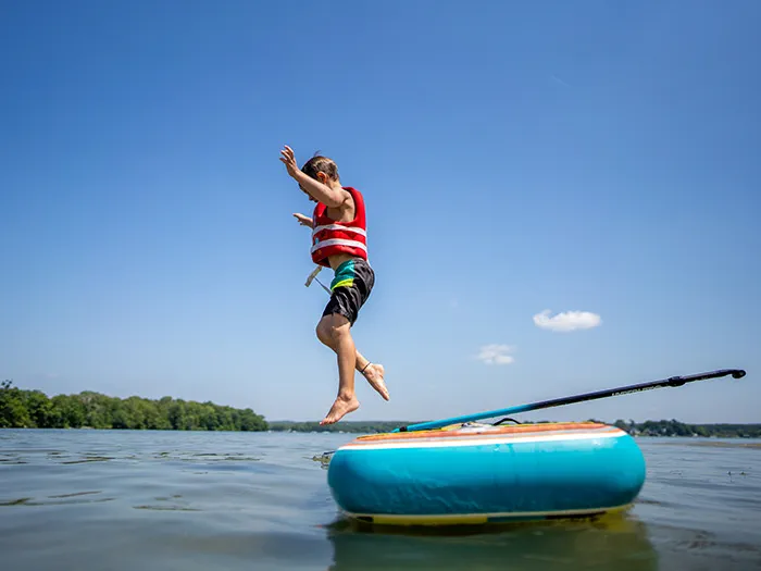A young child wearing a life vest jumping from a raft into a lake with clear blue sky