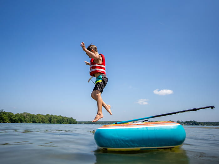 A young child wearing a life vest jumping from a raft into a lake with clear blue sky