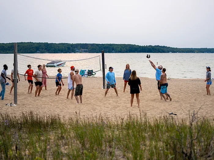 A group of people playing sand volleyball with a lake in the background