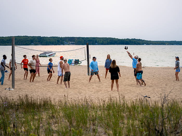 A group of people playing sand volleyball with a lake in the background