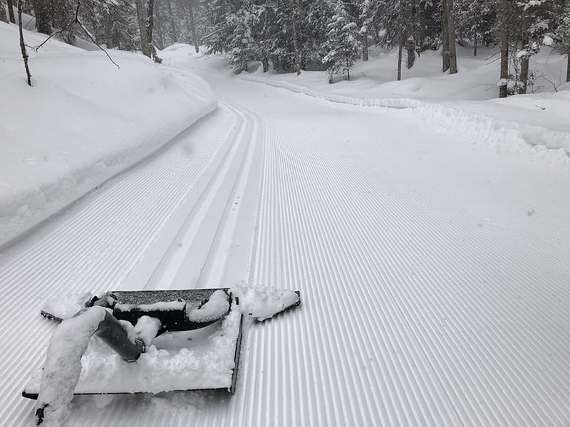 freshly groomed ski trails behind grooming equipment