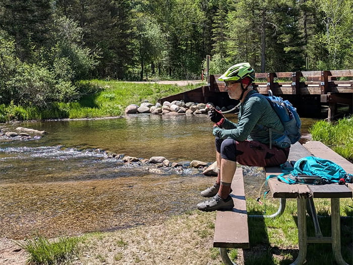 Mountain biker sitting on picnic table near river and bridge