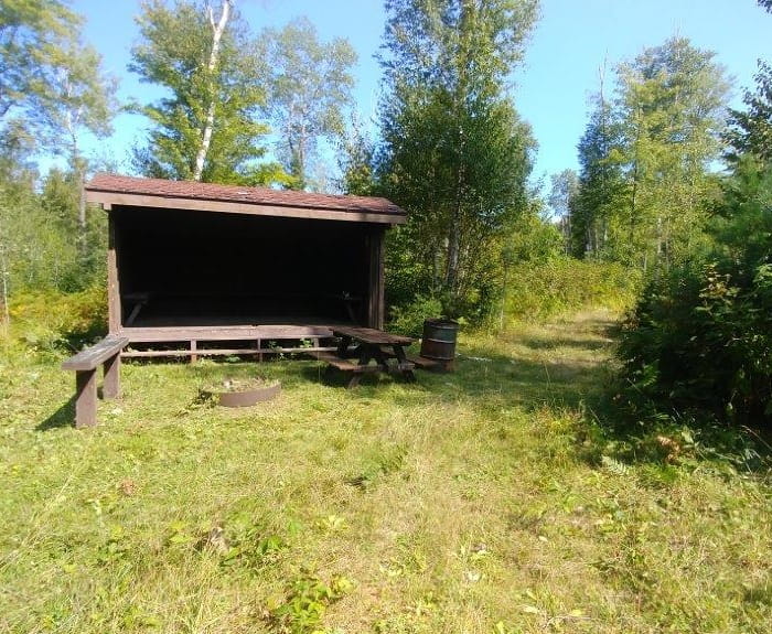 A wooden, three-sided shelter next to a trail