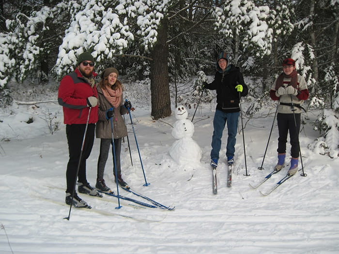 A family on cross-country skis next to a snowman