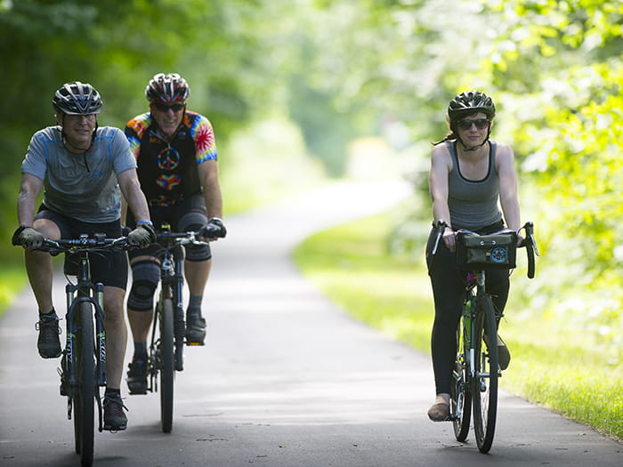 three bikers riding bikes on tree-lined paved trail