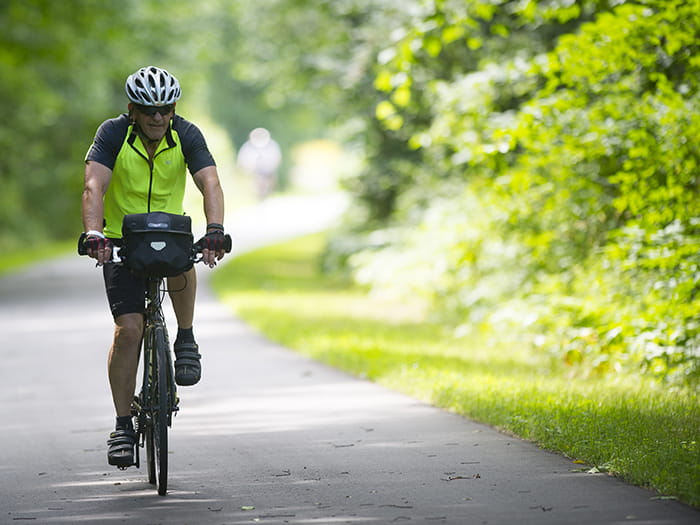 biker riding bike on tree-lined paved trail