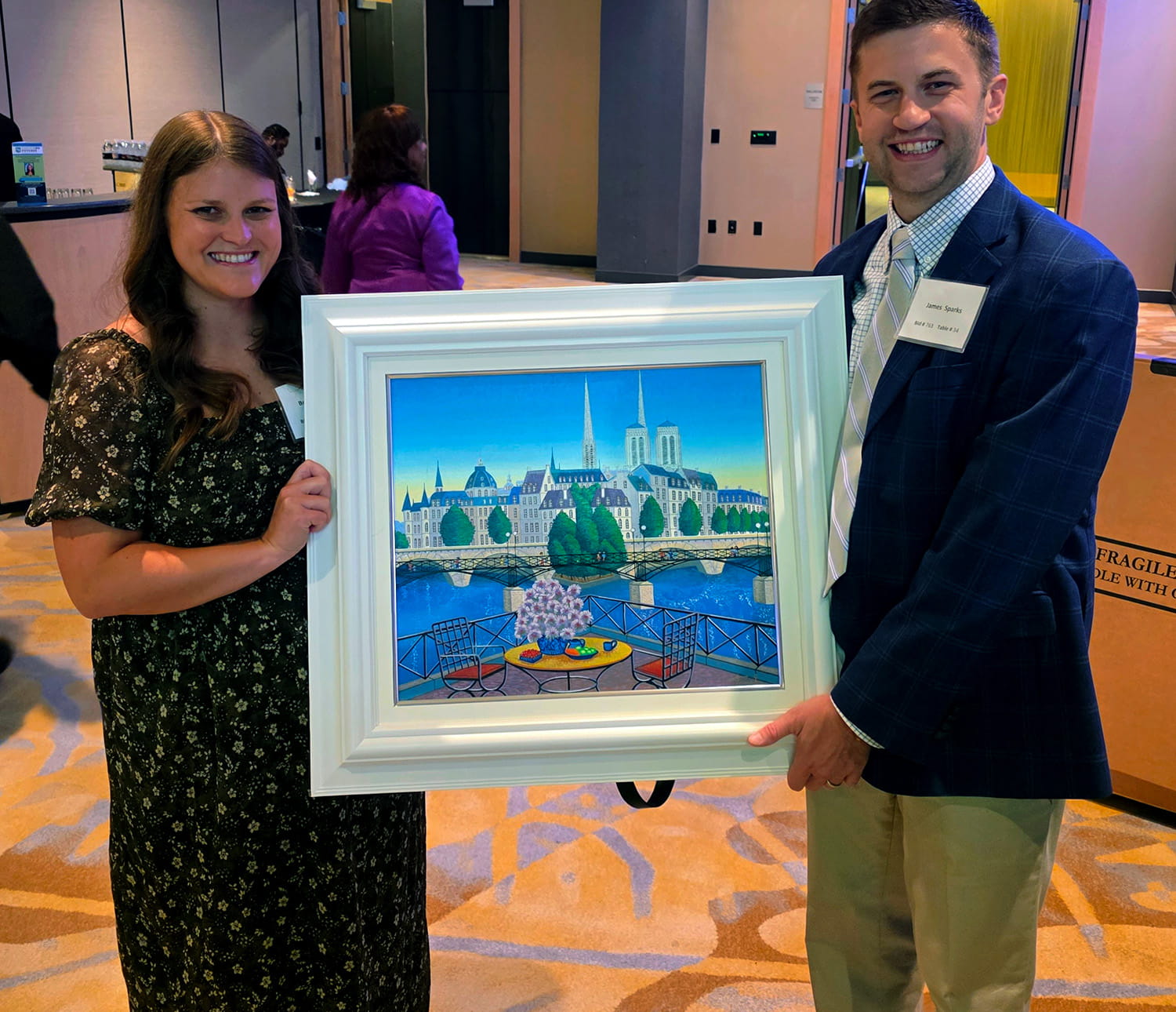 Two happy raffle winners smile as they hold up the artwork they won