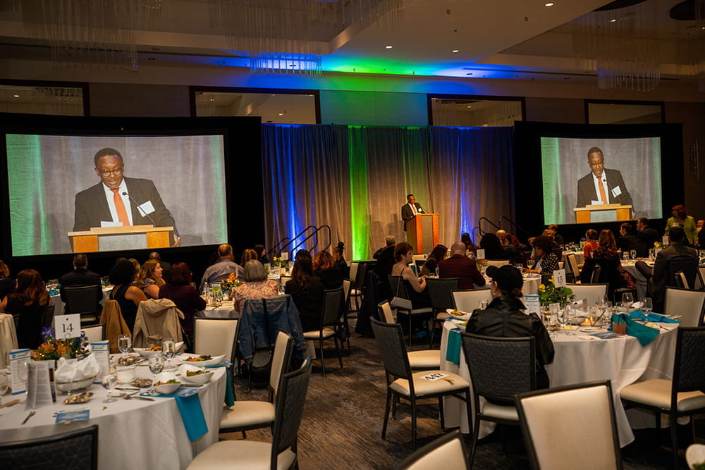 Dr. Tarence Lauchie, Emcee, stands behind the podium as speaks to the crowd