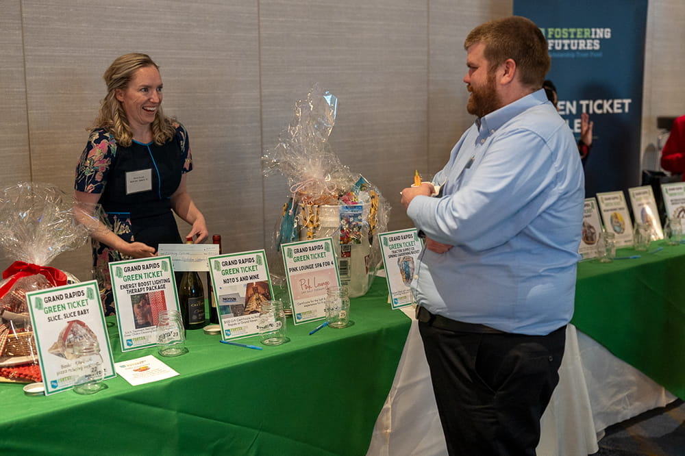 Woman standing behind a table, describing green booth raffle items to guest
