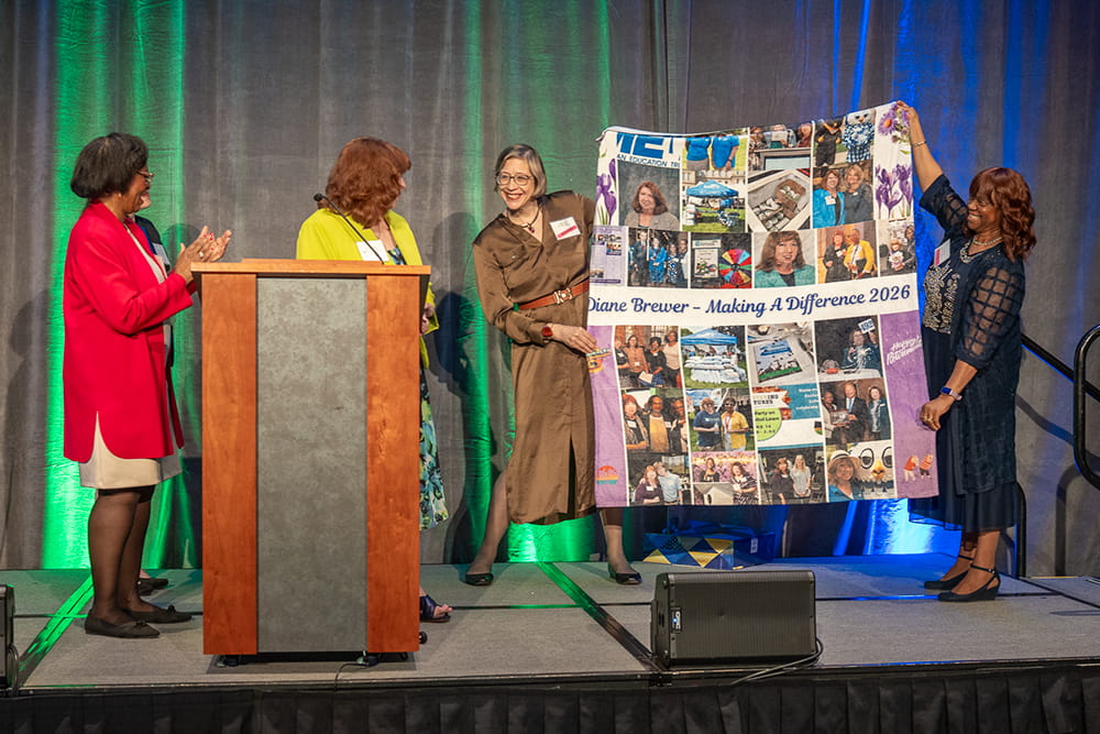 Diane Brewer stands on stage, and is presented a customized blanket, as a thank you by former MET co-workers