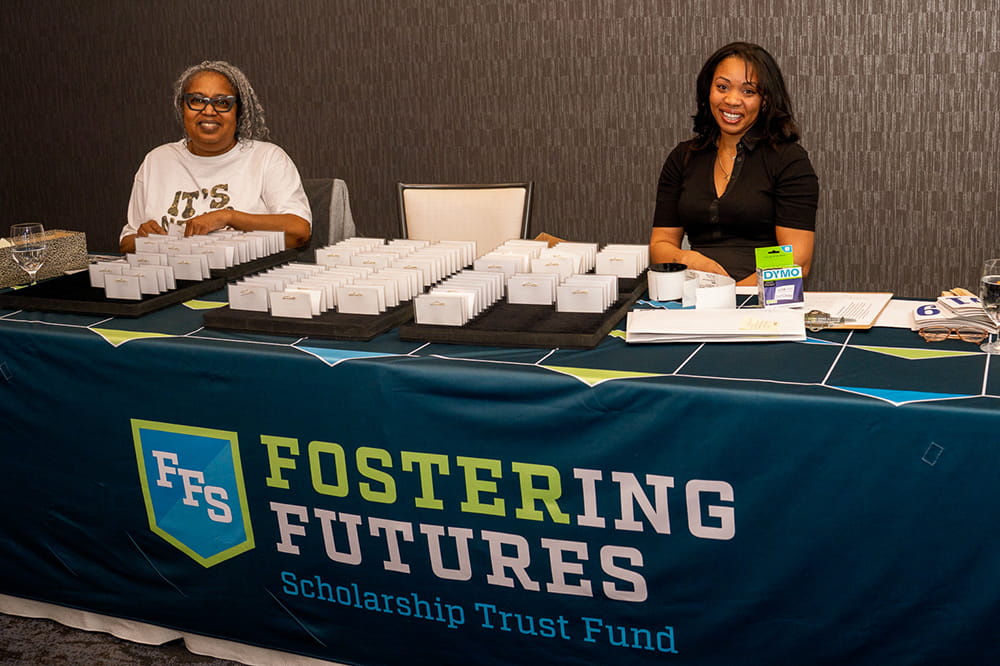 Two women sitting behind a table with all attendees nametags, at the registration table