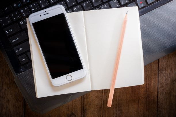 Cell phone sitting on a notebook, sitting on a computer keyboard