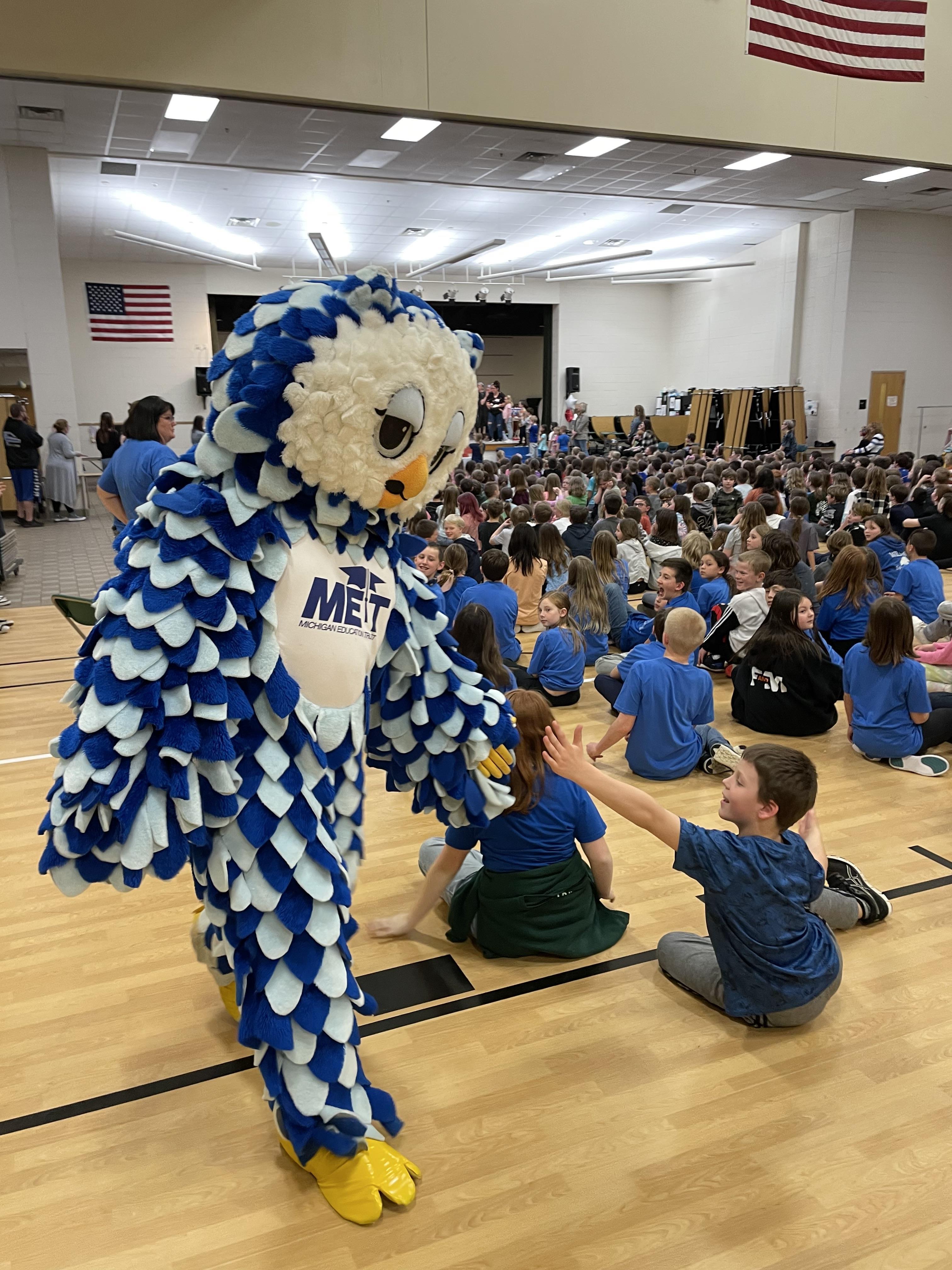 Owl mascot giving a high five to a child sitting at an assembly