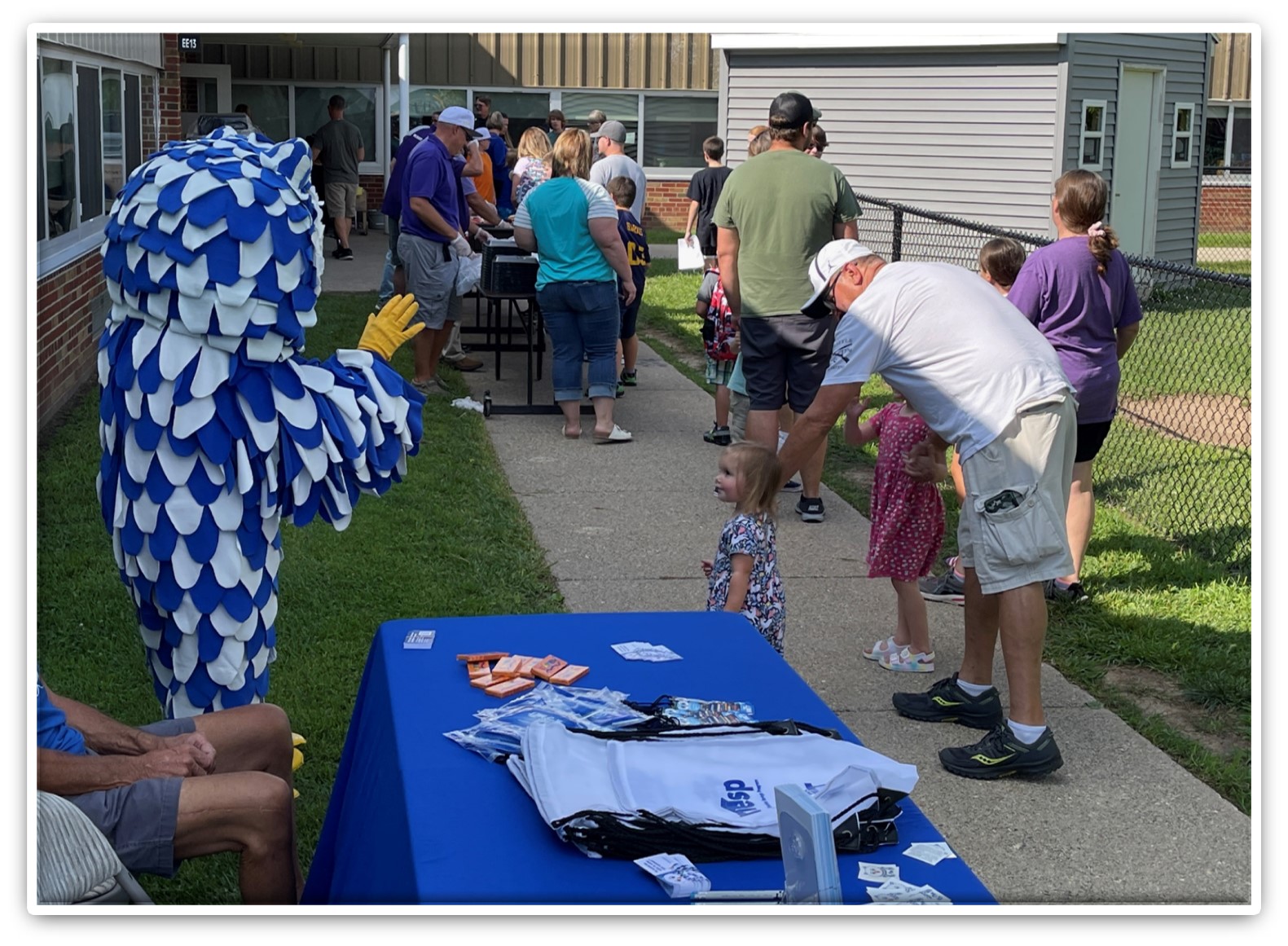 Owl mascot waving at parents and young children while attending an outdoor school event