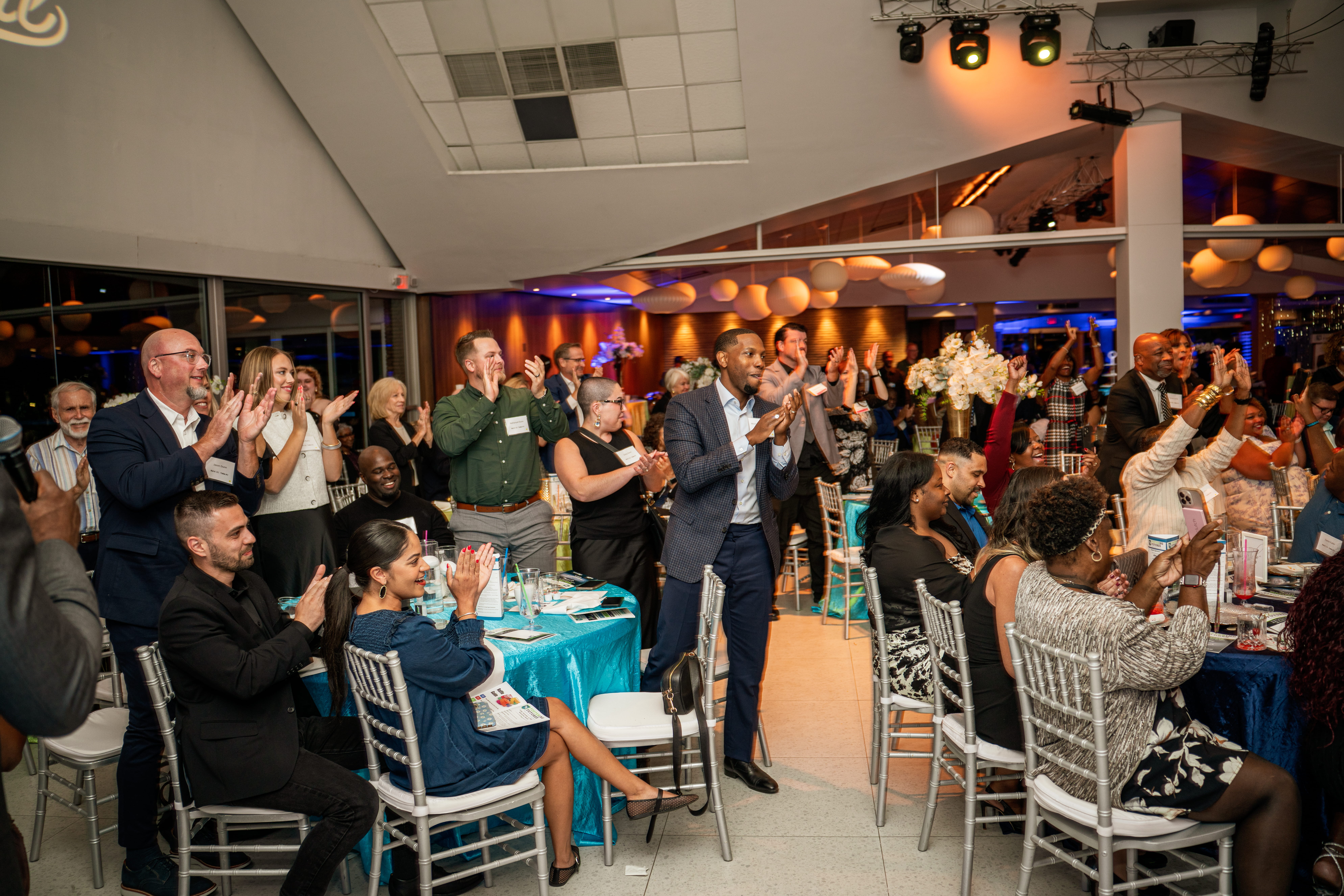 Crowd applauding, some standing, some sitting at a dinner event