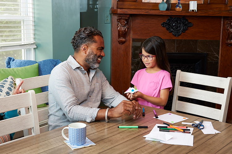 Grandfather sitting the table making a cootie catcher with his granddaughter 