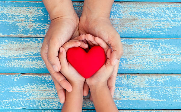 Child's hands holding a heart, wrapped in adult's hands